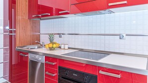 Una cuina moderna amb armaris vermells, electrodomèstics d'acer inoxidable i un plat de fruita al taulell.