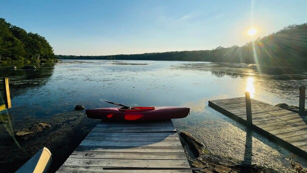 Une jetée en bois s’avance sur une étendue d’eau calme, et un kayak rouge est amarré à son extrémité.