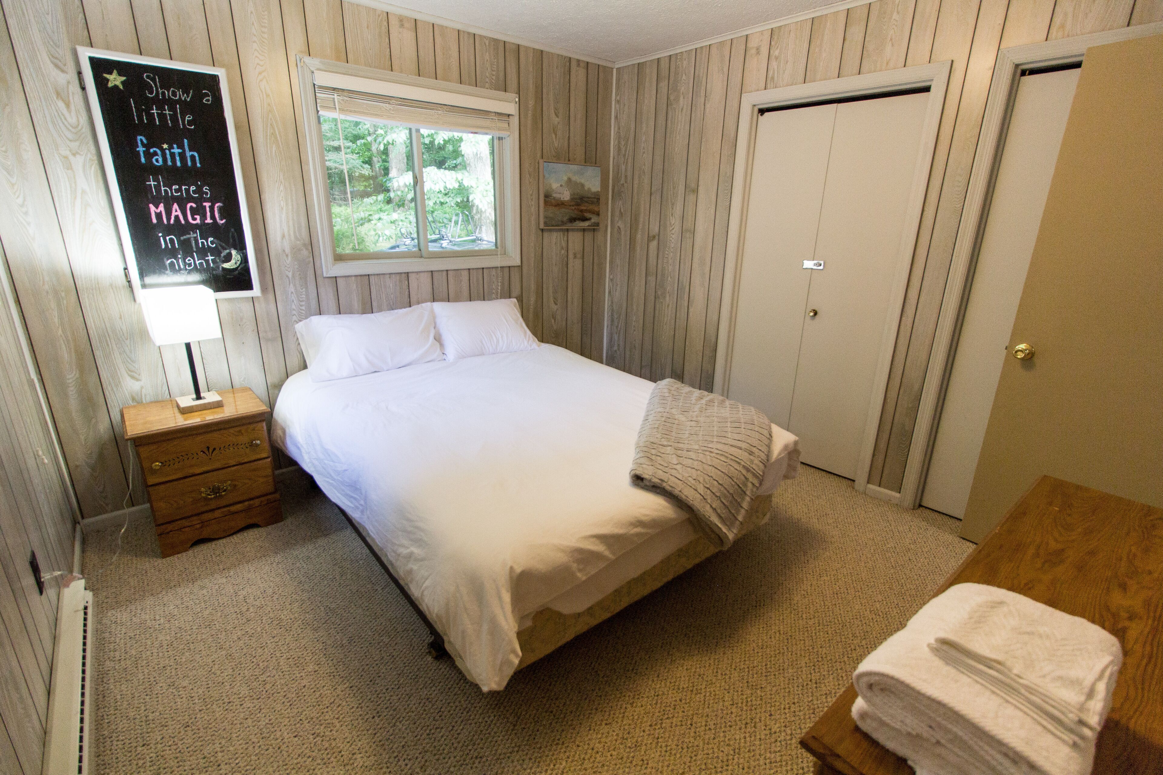 Une chambre bien rangée, avec un lit, une table de chevet, une fenêtre et une porte.