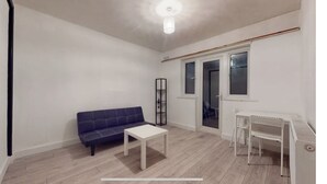 A small, sparsely furnished room with a sofa, a small table, and a desk with a chair. - Amazing 4 bed semi-detached house- close to central (London)