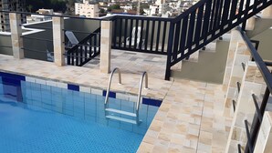 A swimming pool with a tiled deck and a metal staircase leading to a balcony. - 500m da Praia, BIWA Edifício com Piscina, 1garagem, WI-FI, Portaria 24hs, churrasqueira, playground, jardim, Centro do Guarujá, SP (Guarujá)