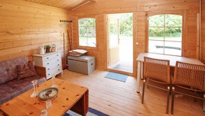 A wooden cabin interior with a sofa, a table with glasses and a tray, a small dresser, a desk with a chair, and large windows with a view of greenery. - 3 bedroom beautiful home in Samsø (Samsø)