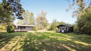 A rustic cabin with a porch and a separate small structure, surrounded by a well-maintained lawn and trees. - 3 bedroom beautiful home in Samsø (Samsø)