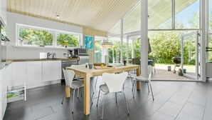 Een moderne keuken met grote ramen, een eethoek met stoelen en uitzicht op de omgeving.