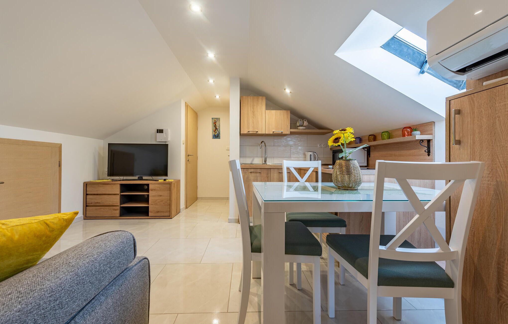 Um apartamento moderno com área de refeições, cozinha compacta e TV na sala de estar.