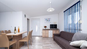 A modern living room with a sofa, a dining table with chairs, a TV, and a decorative piece on the wall. - Awesome apartment in Kavran with WiFi (Kavran)