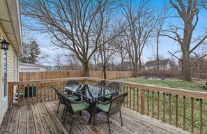 A wooden deck with a glass-top table and wicker chairs, surrounded by a wooden fence and leafless trees. - 10 mins walk to train & town, 15 mins walk to lake! (New Buffalo)