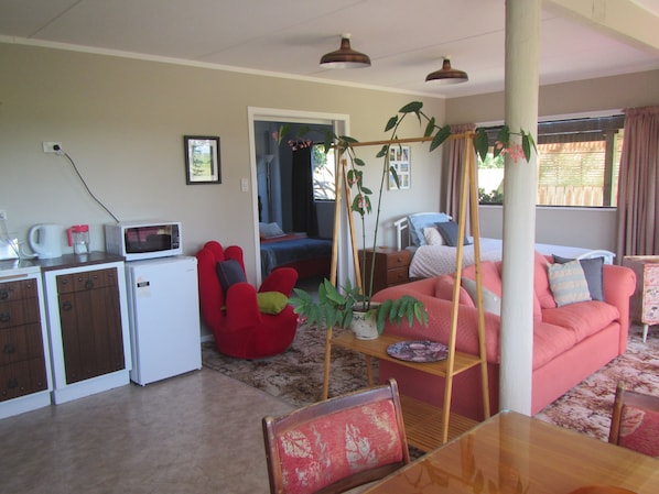 A compact living space with a kitchenette, a red chair, a pink sofa, and a dining table.