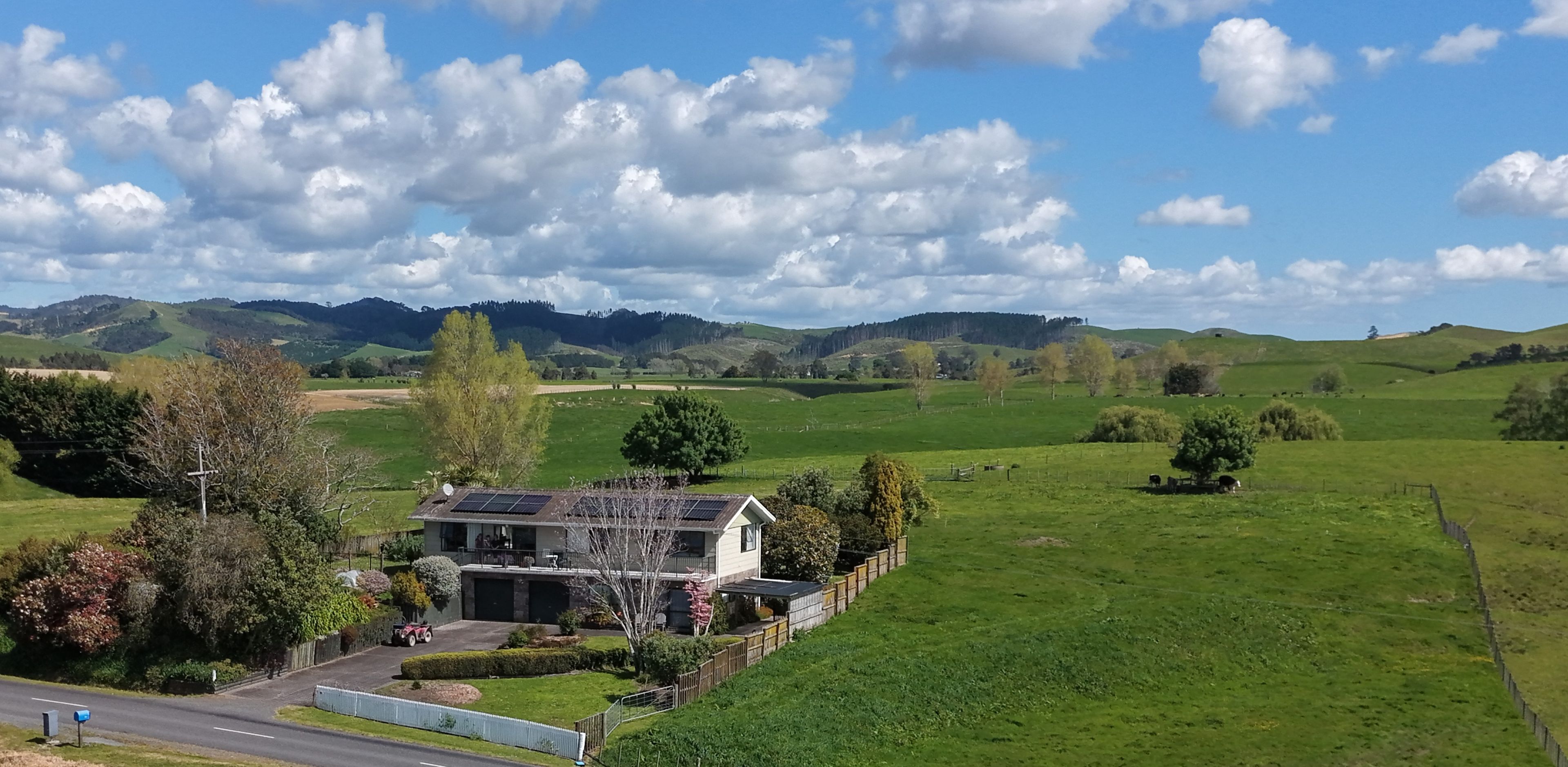A rural house with a fenced yard, surrounded by green fields and hills.