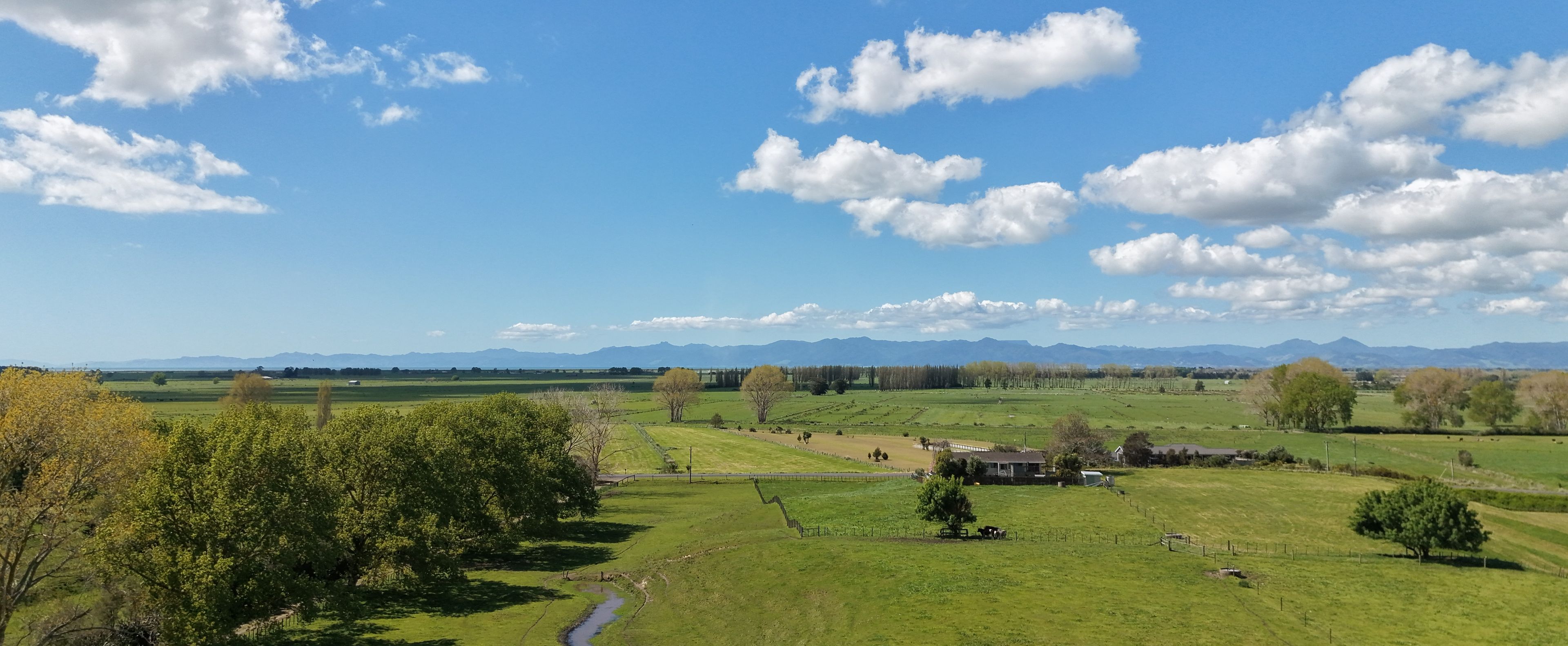 A rural landscape with a house, fields, and mountains in the distance.