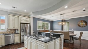 Una cocina moderna con armarios blancos, una isla central, electrodomésticos de acero inoxidable y un comedor con un banco.