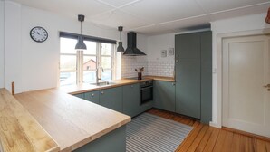 A kitchen with a wooden countertop, a sink, a stove, and a window with a view of a house. - Cozy home in Samsø with WiFi (Samsø)