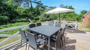 An outdoor deck with a table and chairs, surrounded by a white fence, and a large umbrella providing shade. - Cozy home in Samsø with WiFi (Samsø)