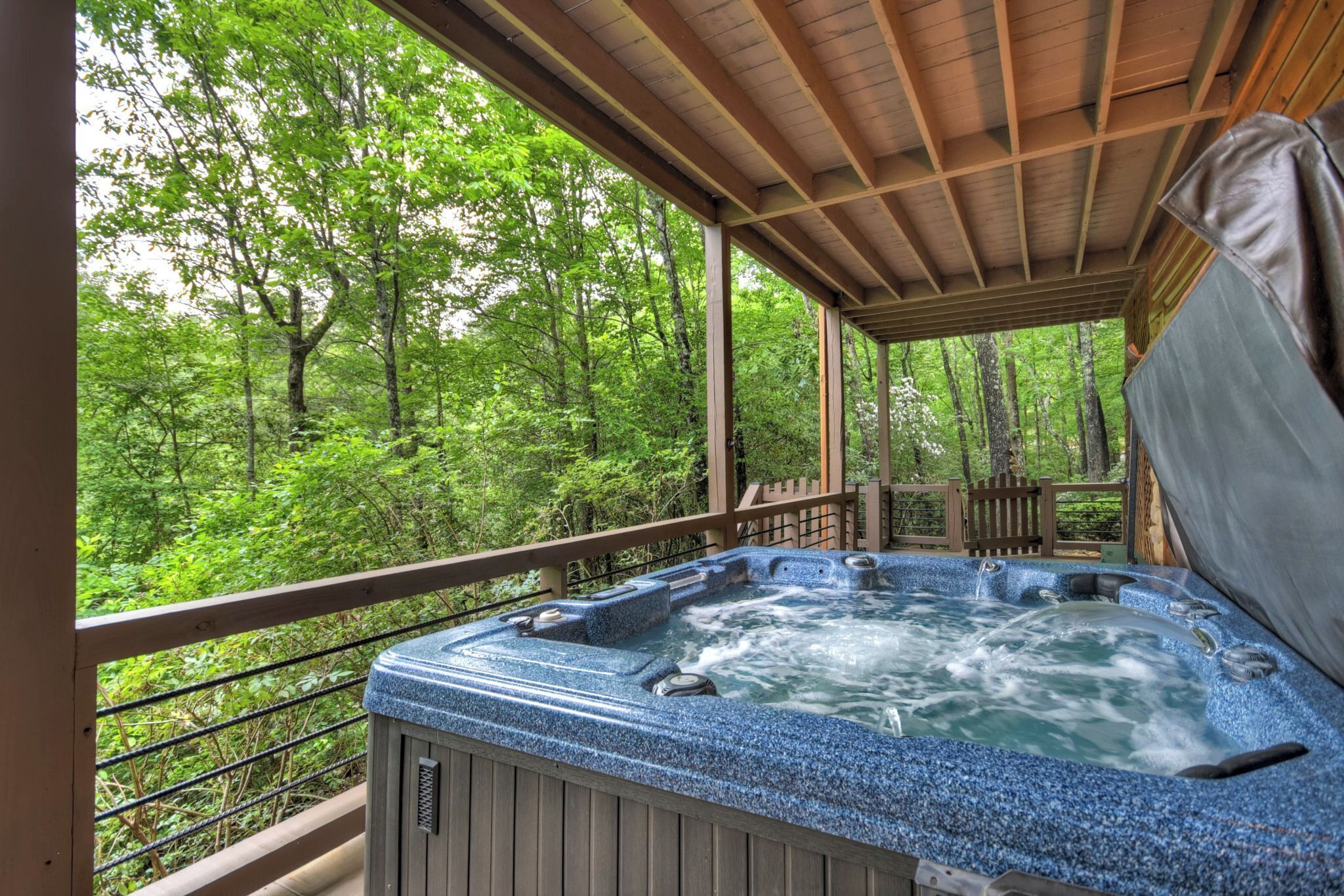 A hot tub on a wooden deck surrounded by lush greenery.