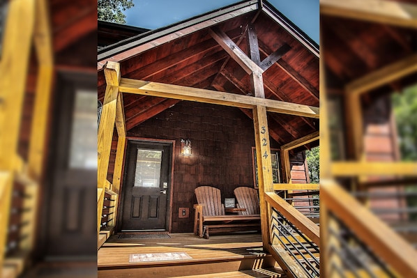 Une cabane en bois avec une véranda, deux fauteuils Adirondack et une porte.