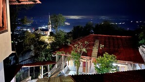 A night view of a building with a red roof, a staircase, and a view of a distant cityscape and a church.