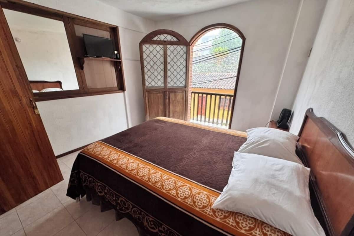 A bedroom with a bed, a wooden headboard, a window with a view, and a door with a mirror.