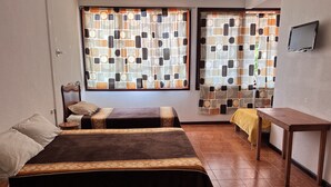A room with two beds, a small table, and a window with patterned curtains.