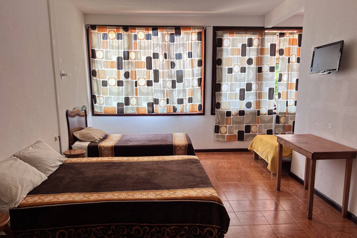 A room with two beds, a small table, and a window with patterned curtains.