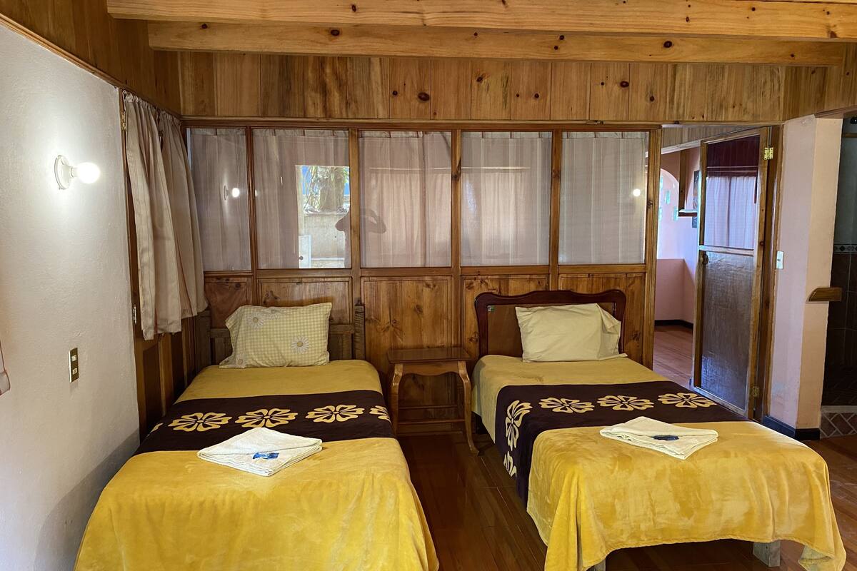 A room with two beds, wooden walls, and a window with curtains.