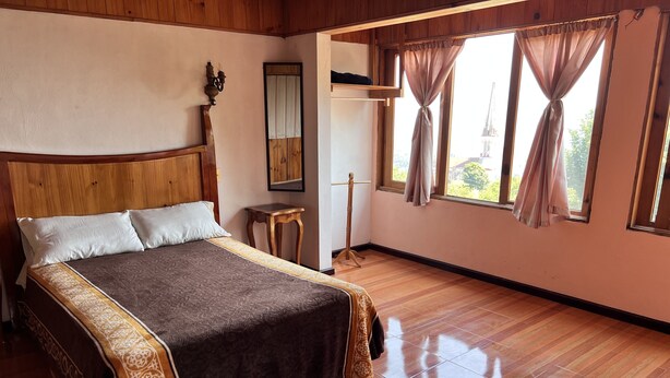 A spacious bedroom with a large bed, wooden headboard, and a view through the window.