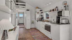 A modern kitchen with white cabinetry, a wooden floor, a colorful rug, and a view of the outside. - Amazing home in Løkken with kitchen (Løkken)