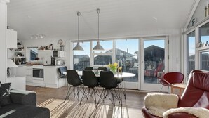A modern kitchen with white cabinets, a dining area with a round table and four chairs, and a large sliding glass door leading to a balcony. - Amazing home in Løkken with kitchen (Løkken)