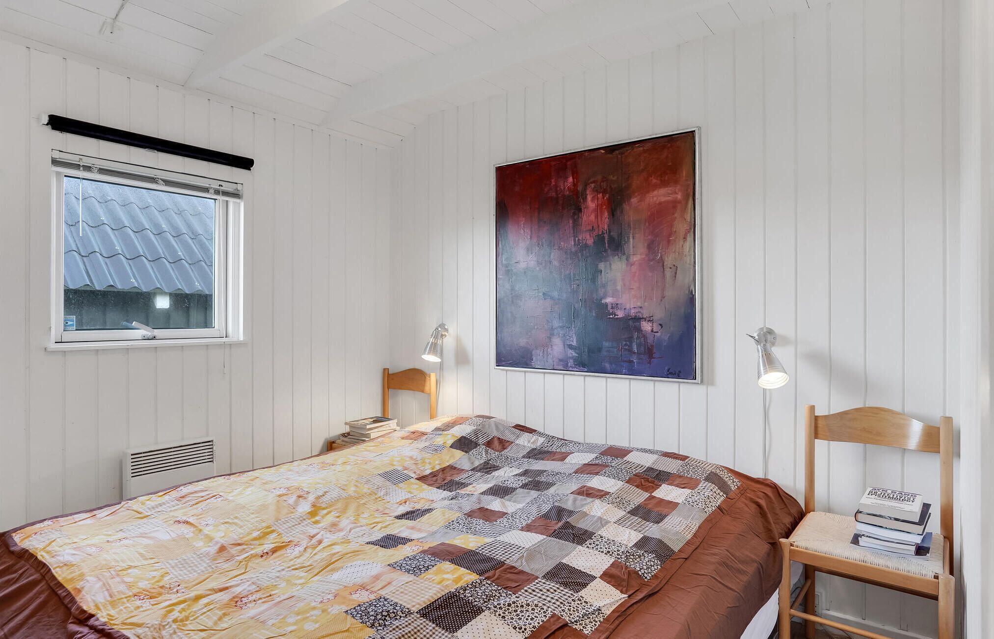 Une chambre avec un grand lit, deux tables de chevet avec des lampes, une fenêtre donnant sur un beau paysage et un grand tableau abstrait accroché au mur.