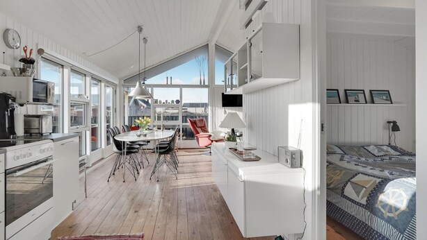 A modern kitchen with a dining area, a red chair, and a bed with a nautical-themed bedspread. - Amazing home in Løkken with kitchen (Løkken)