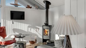 A cozy living room with a fireplace, a comfortable sofa, a red chair, and a television mounted on the wall. - Amazing home in Løkken with kitchen (Løkken)