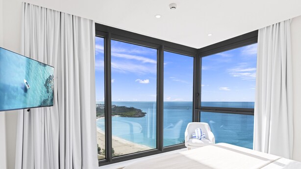Une chambre d’hôtel moderne dotée d’une grande fenêtre donnant sur la mer et une falaise.