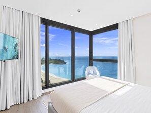 A bedroom with a large window offering a view of the ocean and a beach. - A-1601 Stunning 3 bedroom ocean view (Cupecoy)