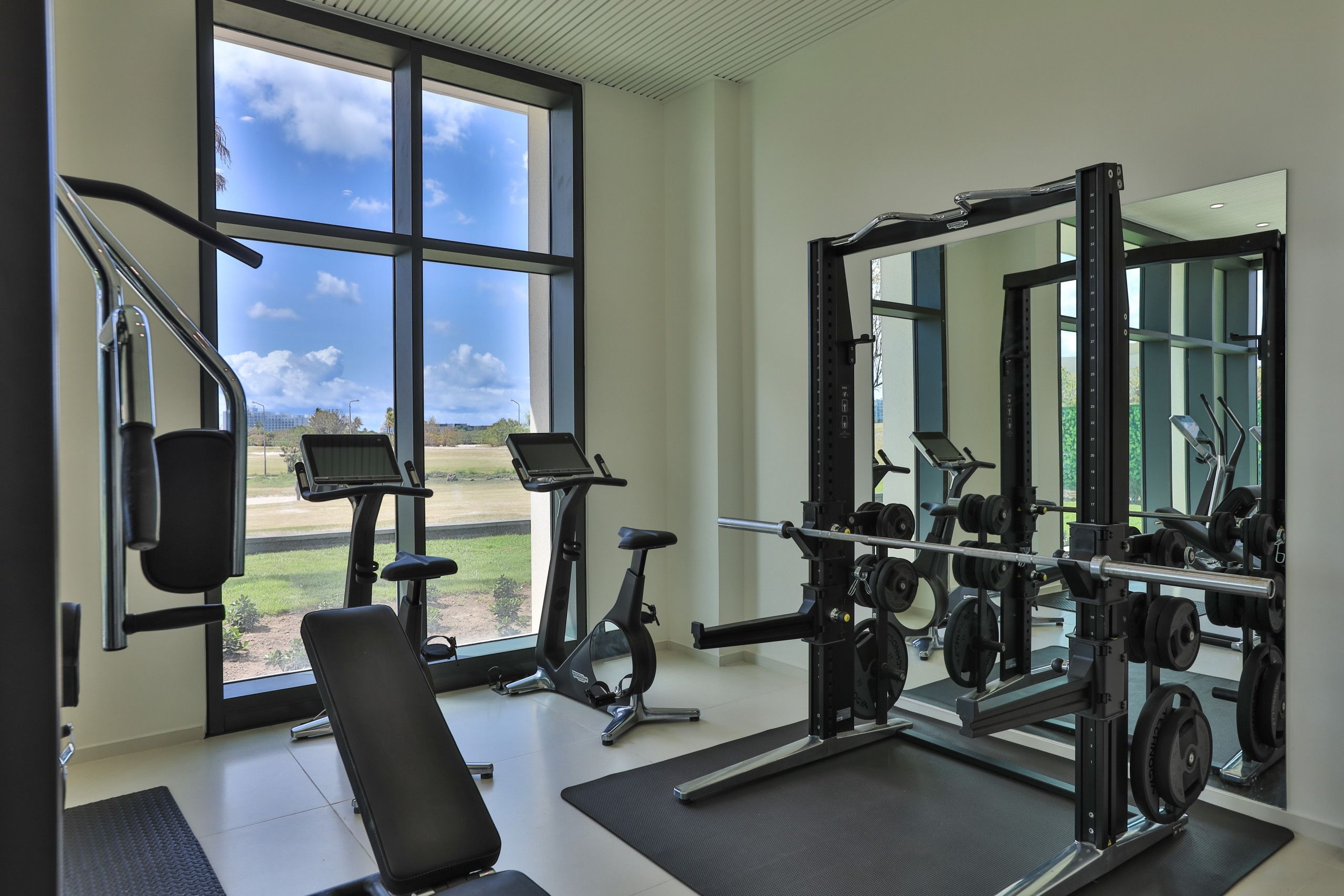 A gym with exercise equipment, a bench, and a large window with a view of a green landscape.