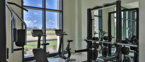 A gym with exercise equipment, a bench, and a large window with a view of a green landscape.