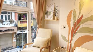 A room with a wooden chair, a small table, and a bed. There is a window with a view of the street and shops. - Hanoi Old Quarter Center - 1BR Studio - Big window & Balcony & Private Bathroom (Hà Ni)