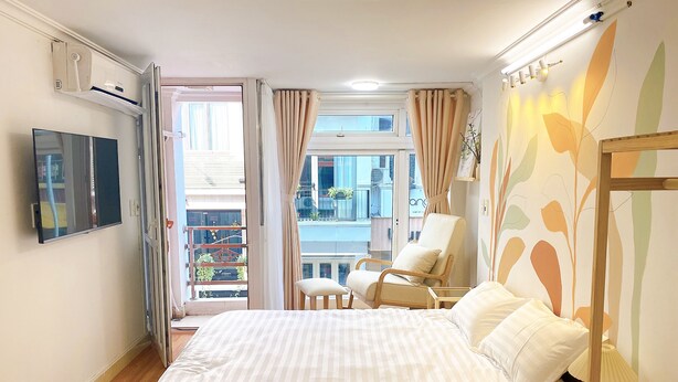 A bedroom with a bed, a chair, a TV, and a balcony with curtains. - Hanoi Old Quarter Center - 1BR Studio - Big window & Balcony & Private Bathroom (Hà Ni)