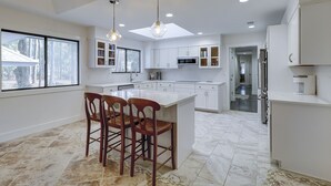 Uma cozinha moderna com armários brancos, uma ilha central com banquetas e iluminação pendente.