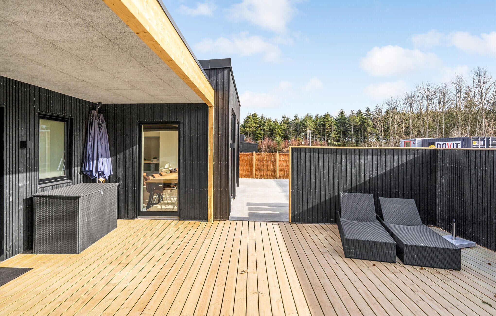 Eine moderne Außenterrasse mit Holzboden, schwarzen Wänden und einer Glastür zu einem Innenraum.