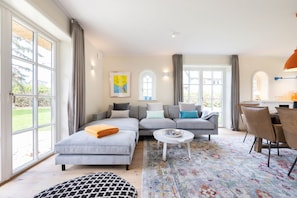 Una sala moderna con sofá, reposapiés, mesa de centro y comedor.