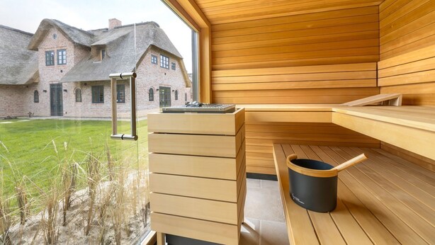 A sauna room with wooden benches and a large window overlooking a grassy area and a brick building.