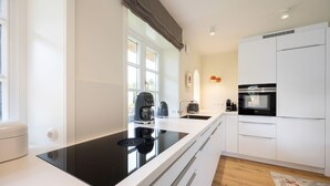 A modern kitchen with a black induction cooktop, white cabinets, a built-in oven, and a coffee maker.