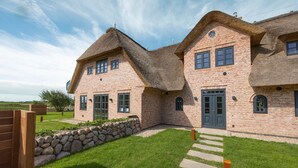 A large brick house with a thatched roof, a stone wall, and a grassy lawn.
