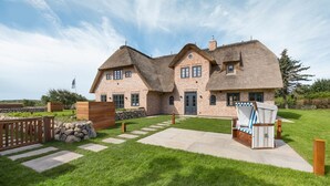 A large brick house with a thatched roof, a stone pathway, and a wooden deck.