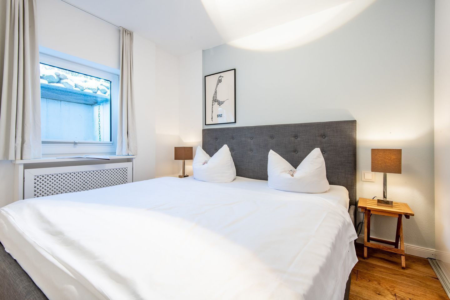 A hotel room with a large bed, two bedside tables with lamps, a window with curtains, and a framed picture on the wall.