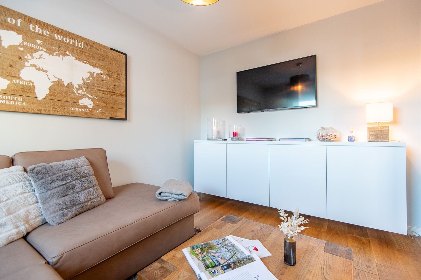 Uma sala de estar moderna com um sofá marrom, um armário branco e uma televisão de tela plana fixada na parede.
