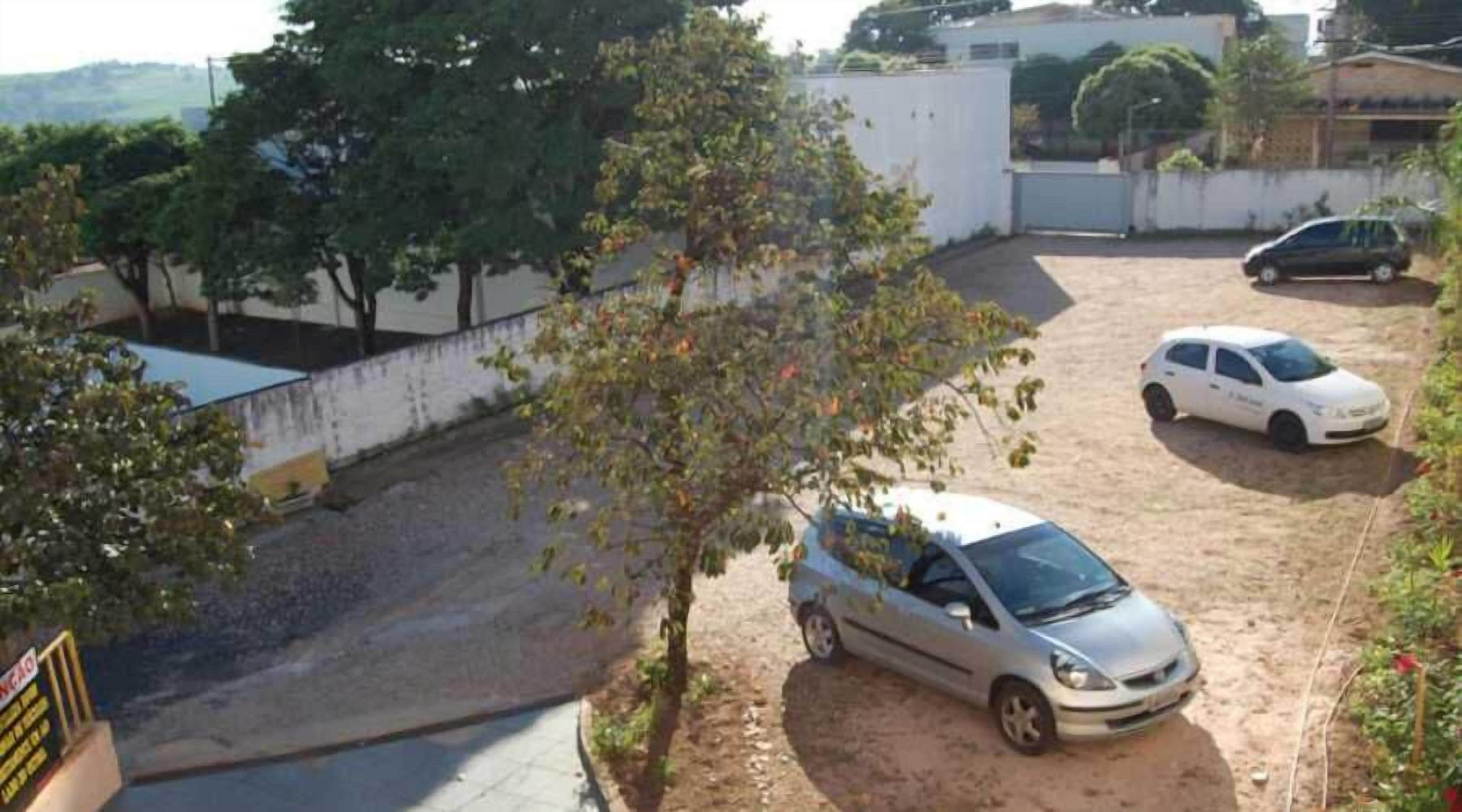 Uma área de estacionamento com um caminho de terra que leva a um edifício. Dois carros estão estacionados, um branco e um prateado.