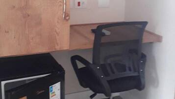 Un pequeño espacio de oficina con una puerta de madera, una silla de oficina negra y un archivador negro.