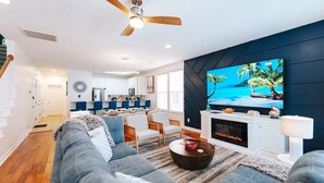 A modern living room with a large TV, a ceiling fan, and a fireplace. - Beach Family Oasis · Year-Round Heated Pool · Steps to Sand · Dog Friendly (Surfside Beach)