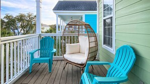 A wooden deck with turquoise chairs and a wicker chair with a cushion.