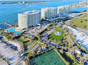 Un hotel de gran altura con varios pisos, piscina, canchas de tenis y un puerto deportivo.